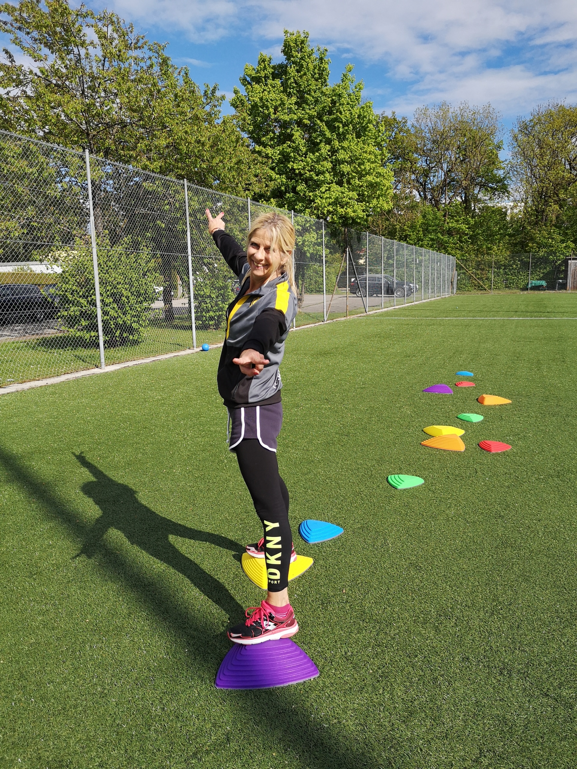 Tina Rauhut balanciert auf dem Sportplatz des TSV Waldtrudering auf bunten Flusssteinen, streckt die Arme zur Seite und lacht in die Kamera.